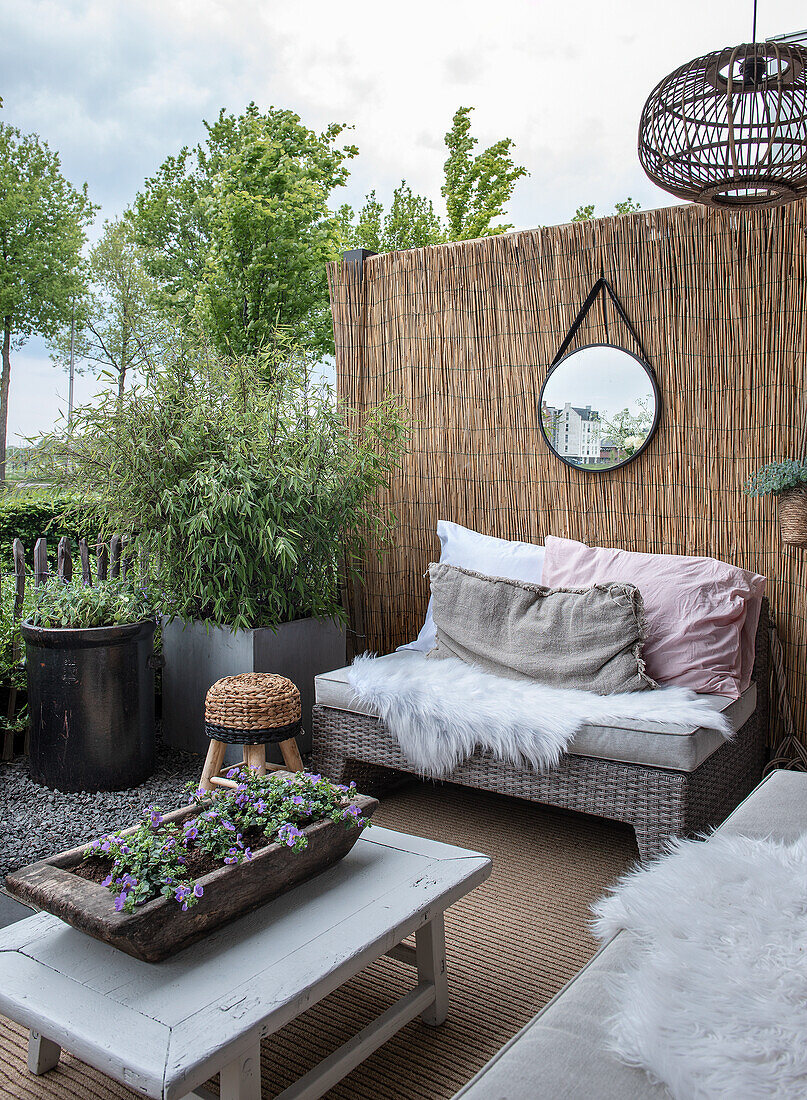 Gemütliche Terrasse mit Bambuswand, Rattanmöbeln und Blumenarrangement