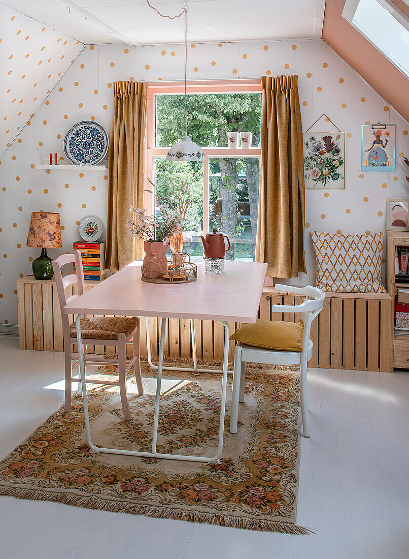 Room with dining table in pink, white chairs with seat cushions, vintage carpet and walls with dot pattern