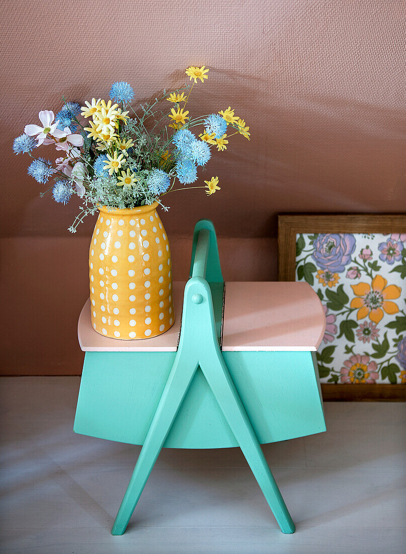 Blumen in gelber Vase mit weißen Punkten auf bemaltem Vintage-Nähkästchen