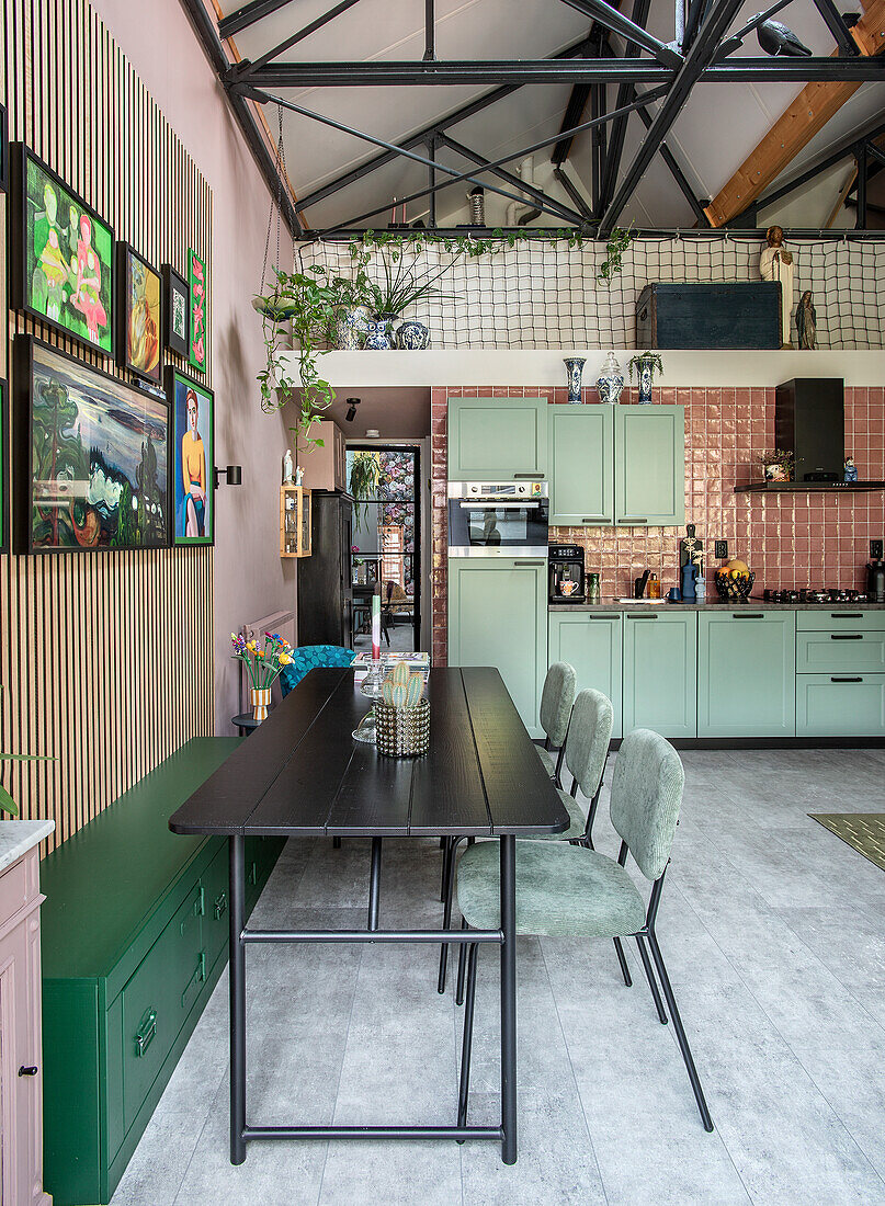 Open-plan kitchen with green cupboards, black dining table and artwork on the wall