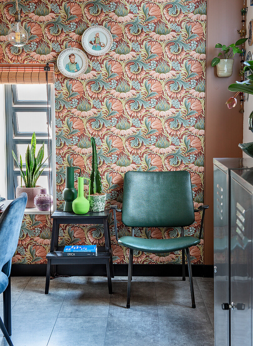 Green chair, stool and plants in front of retro-style patterned wallpaper