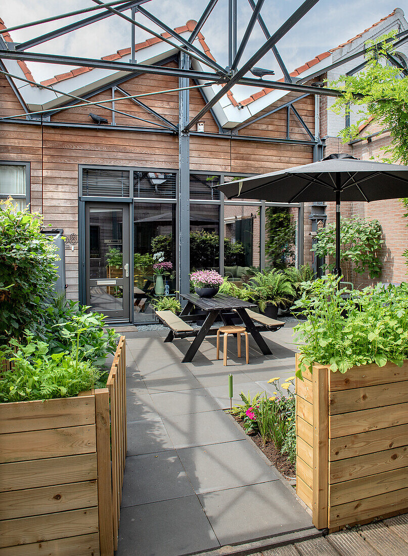 Moderne Terrasse mit Holzelementen, Pflanzen und schwarzem Gartentisch