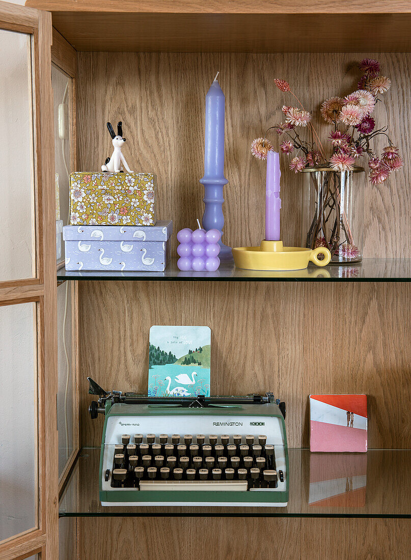 Shelf with typewriter, candles and decorative boxes on glass shelf