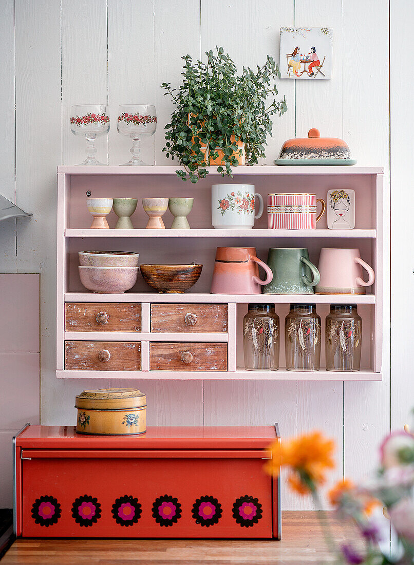 Shelf with crockery and potted plant above red bread box in the kitchen