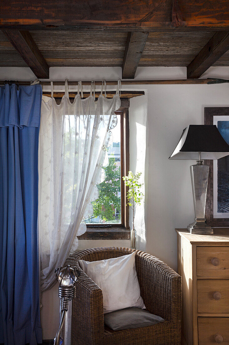 Rattan armchair with cushions in front of window with blue curtain and white curtain