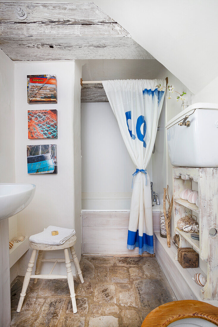 Small bathroom with shower curtain and natural stone floor, maritime artwork