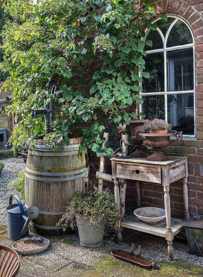 Rustic garden table with flower pot and old wine barrel pump in front of brick façade