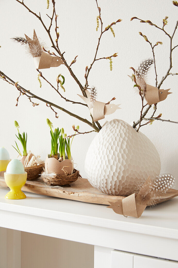 Branches in a white vase with DIY paper birds and feathers on a wooden tray