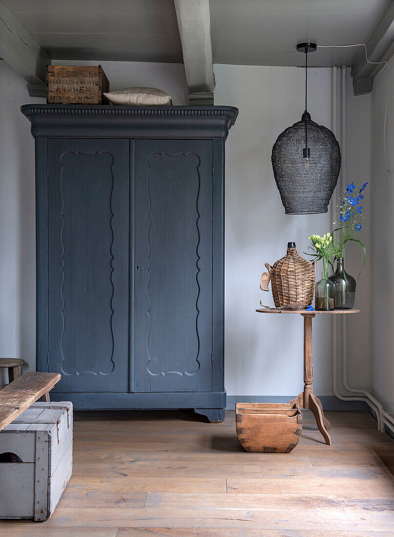 Blaugrauer Bauernschrank und kleiner Beistelltisch mit Blumenvasen in rustikalem Wohnzimmer