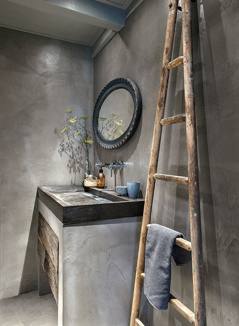 Rustic bathroom with concrete walls, ladder towel rail and round mirror