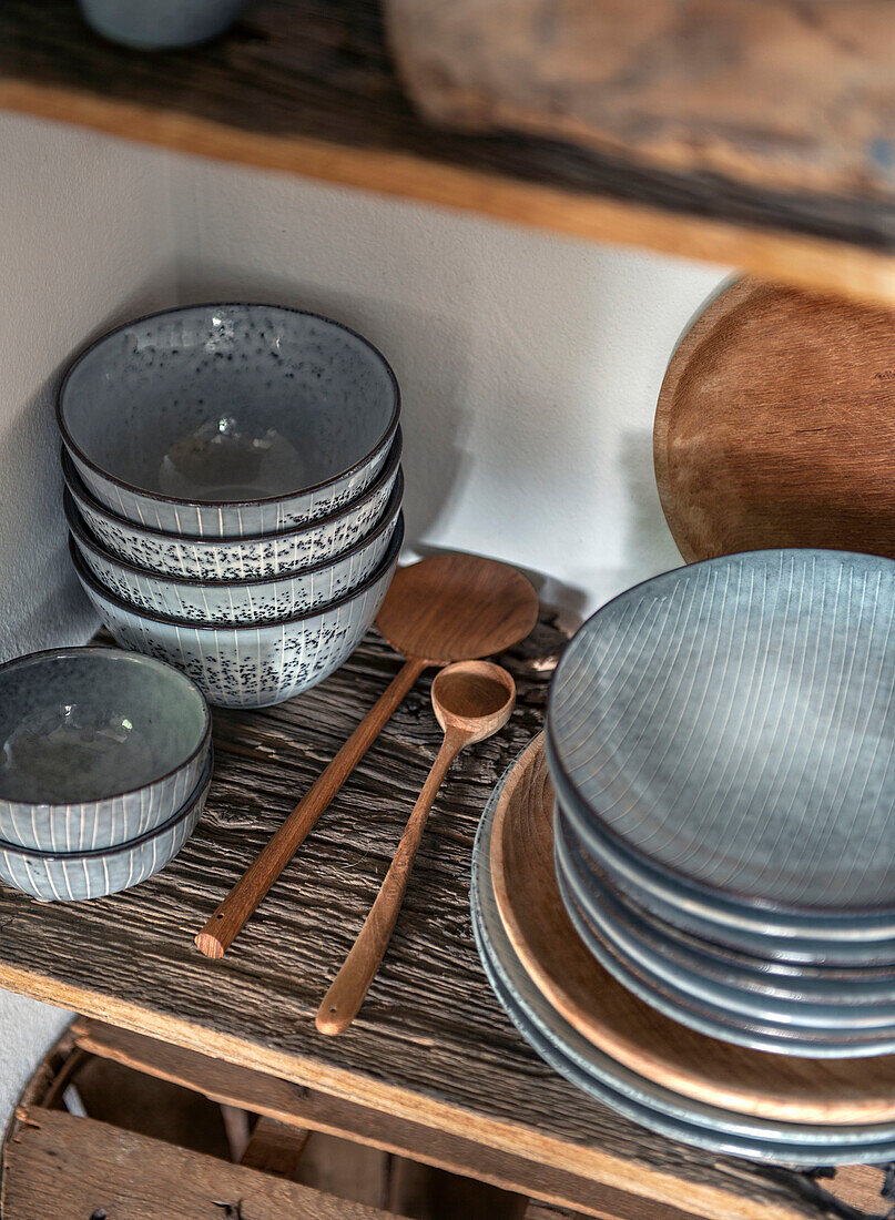 Grey ceramic bowls and plates on a rustic wooden shelf