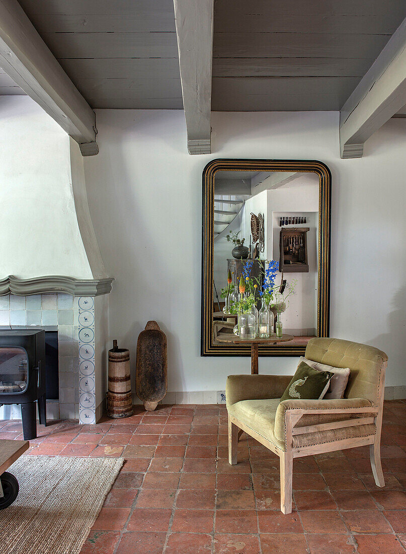 Armchair with wooden frame in front of wall mirror and country-style fireplace