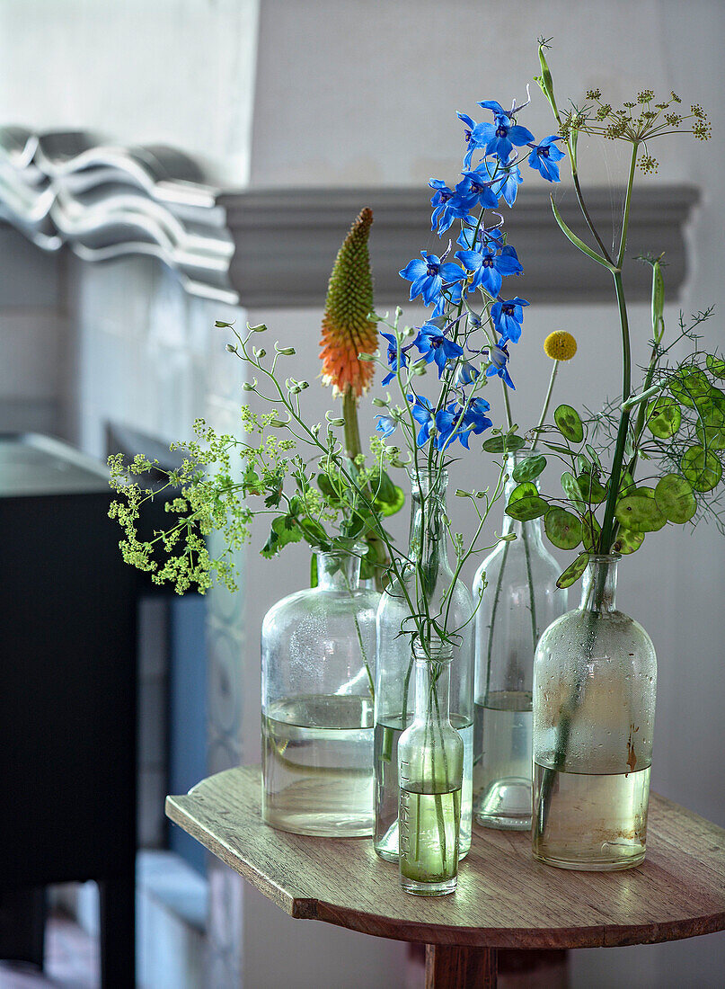 Various wildflowers in glass bottles on a small wooden table