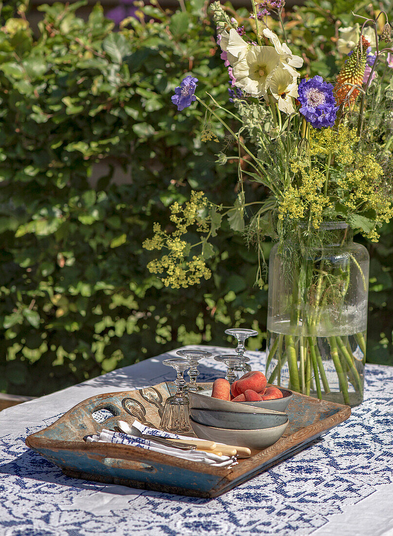 Bouquet of flowers in a glass vase and tray with candle holders and fruit on a lace tablecloth in the garden