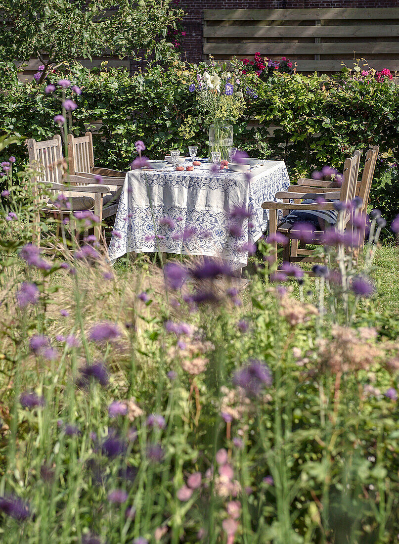 Flower garden with laid table and wooden furniture in the summer