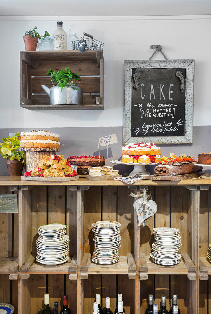 Kuchentheke mit verschiedenen Torten und Kuchen vor rustikalem Holzregal