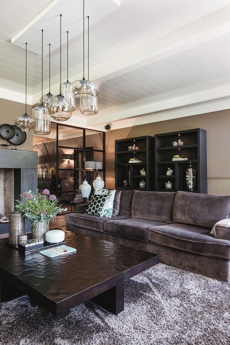 Living room with brown velvet sofa, hanging glass pendant lights and display cabinets