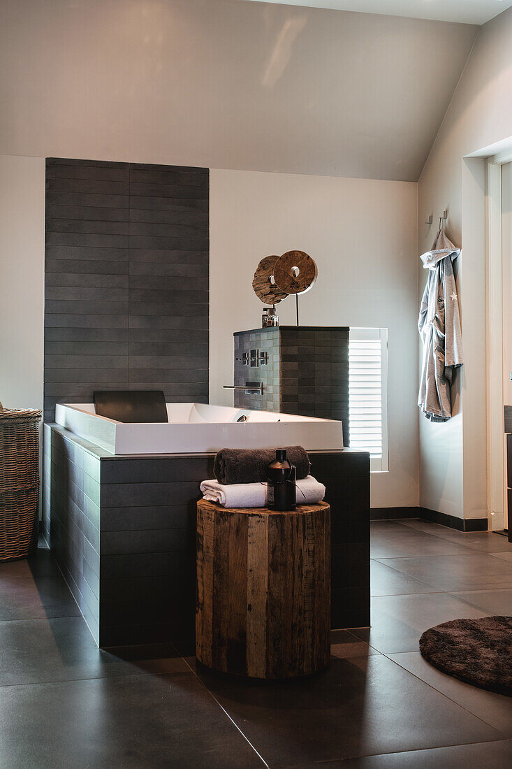 Modern freestanding bathtub with wooden decor and dark tiles