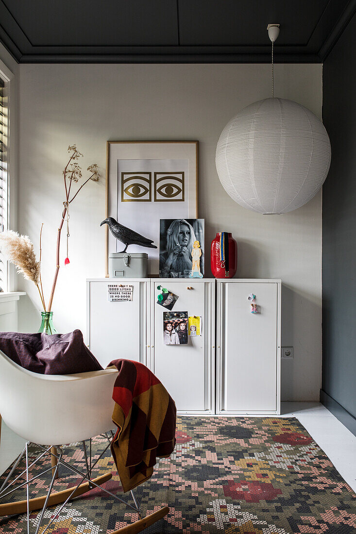 White filing cabinet decorated with postcards, picture wall and designer chair