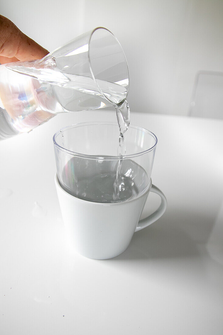 Wasser wird in ein transparentes Glas in einer weißen Tasse gegossen