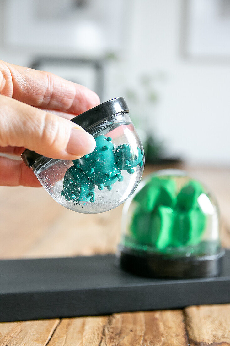 Hand holding snow globe with cactus on wooden table