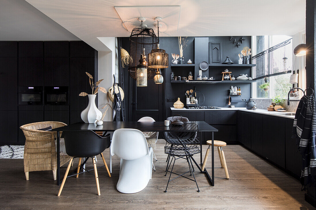 Modern kitchen in black and white with dining table, decorative pendant lights and various chairs