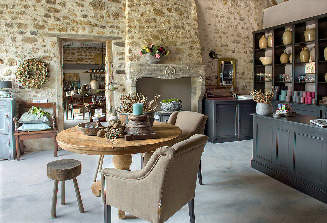 Round wooden table in open-plan kitchen with natural stone wall in French farmhouse