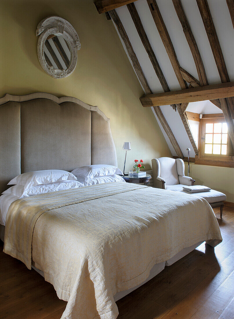 Doppelbett mit hohem, gepolstertem Betthaupt in rustikalem Dachgeschosszimmer in Beigetönen