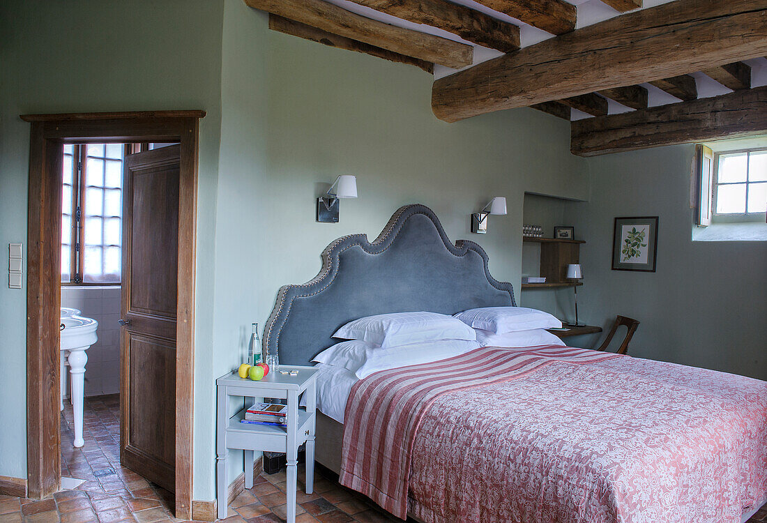 Doppelbett mit hohem, gepolstertem Betthaupt in rustikalem Schlafzimmer mit Deckenbalken