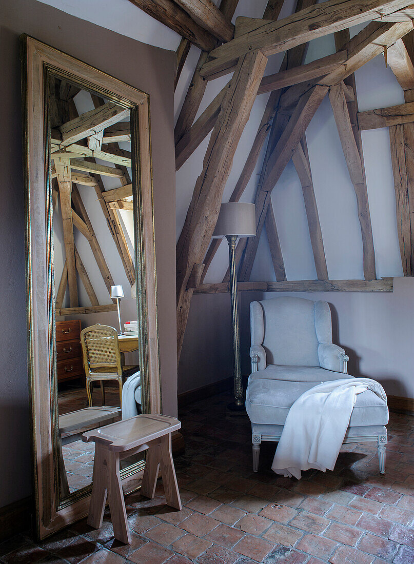 Cozy reading corner and large wall mirror in rustic room with wooden beams