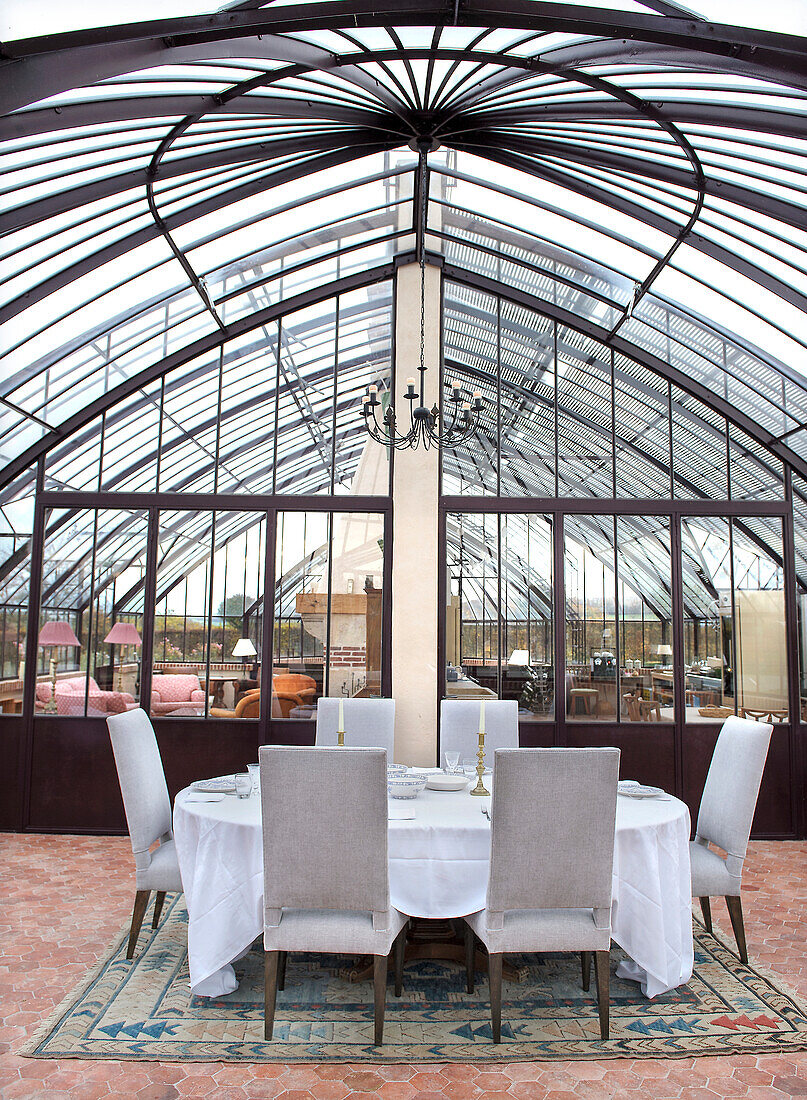 Festively laid table in elegant conservatory with glass roof and chandelier