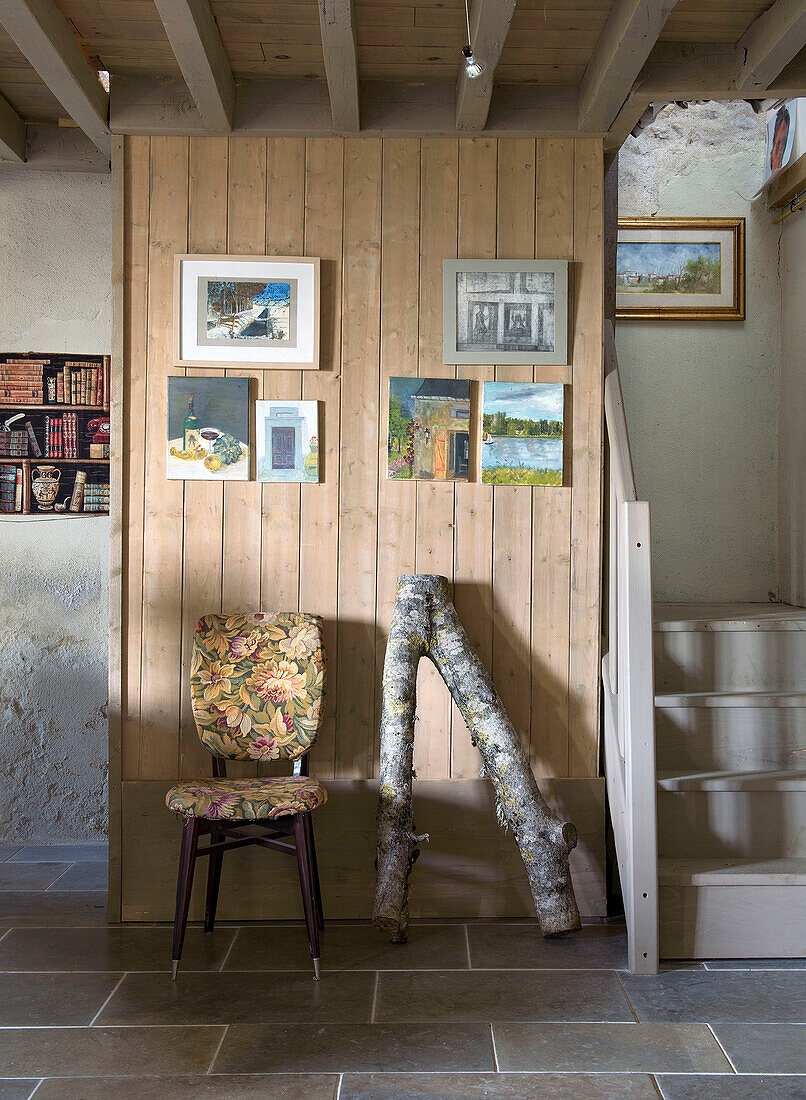 Stuhl und Ast vor Holzwand mit Bildern
