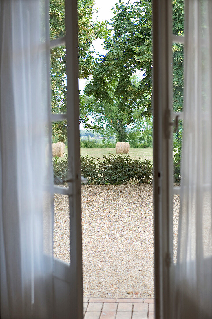 Blick durch geöffnete Fenstertüren auf Kiesterrasse und Landschaft