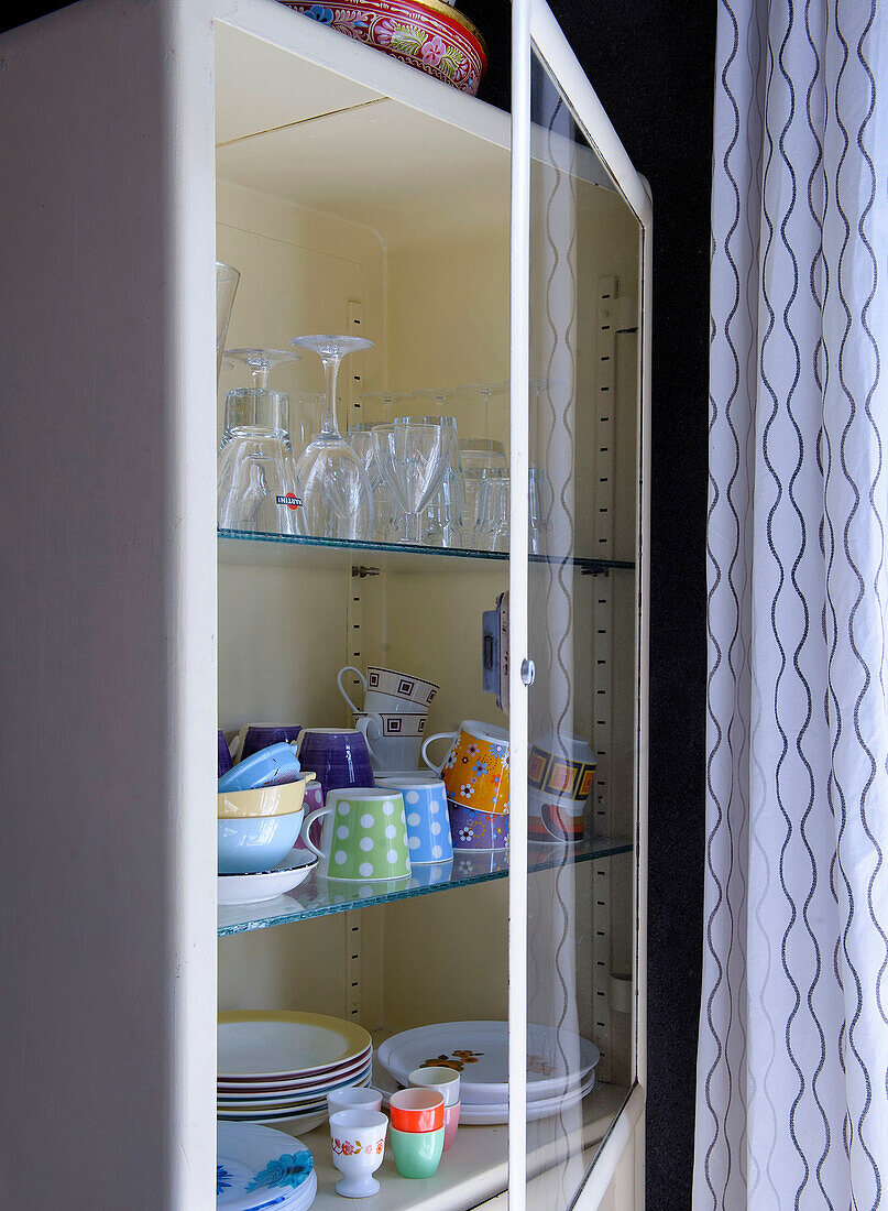 Colorful crockery in cupboard with open glass door