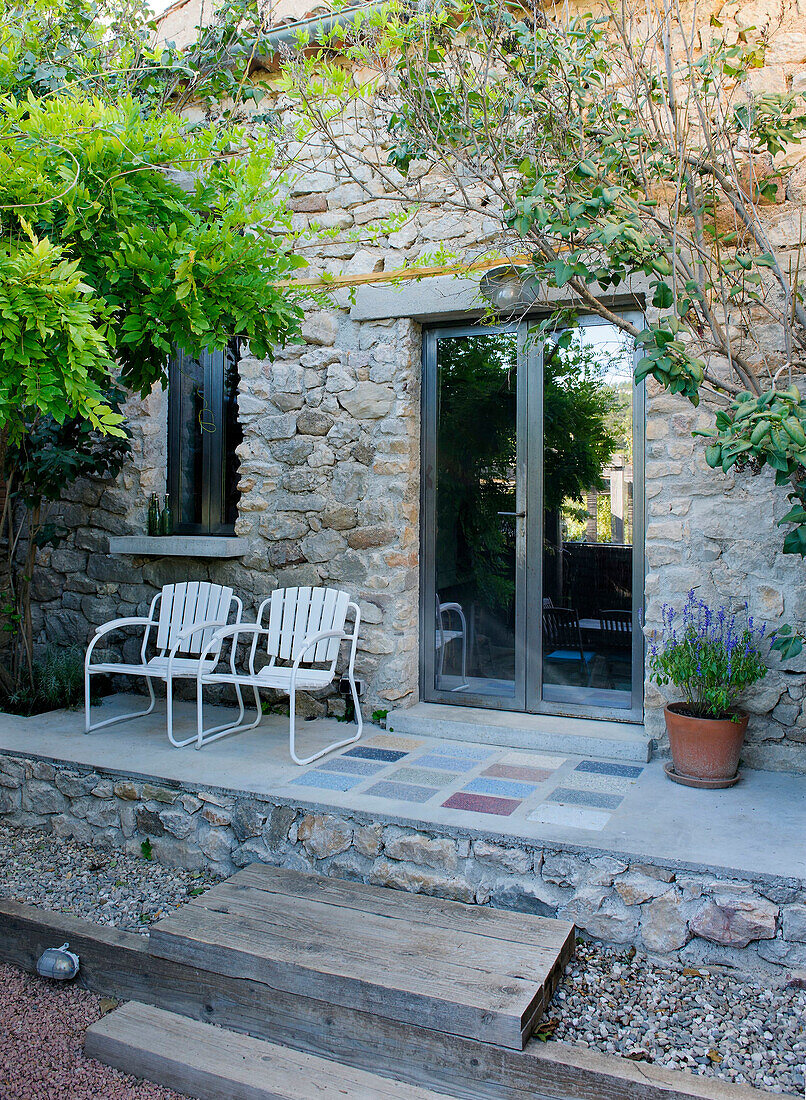 Two chairs on terrace in front of natural stone house