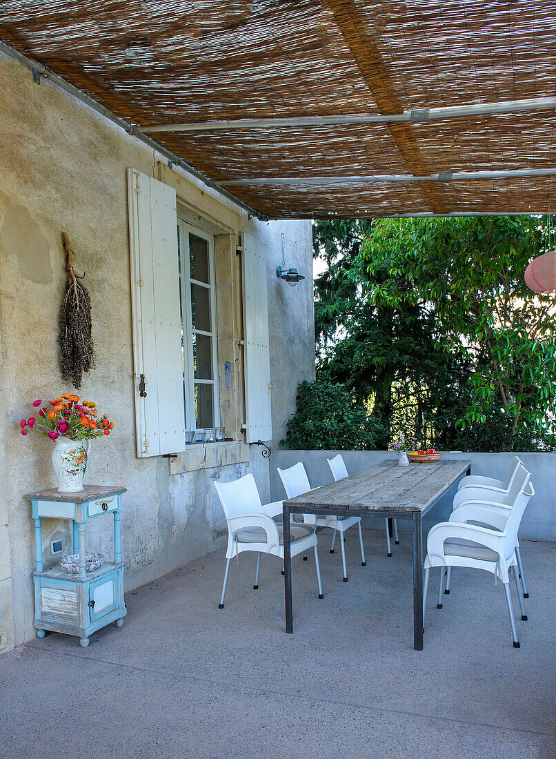 Rustikaler Tisch mit modernen Stapelstühlen auf überdachter Terrasse
