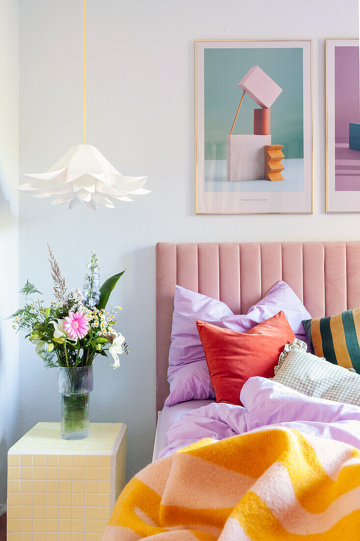 Bedroom with pastel-colored bed, pictures and bouquet of flowers on modern bedside table