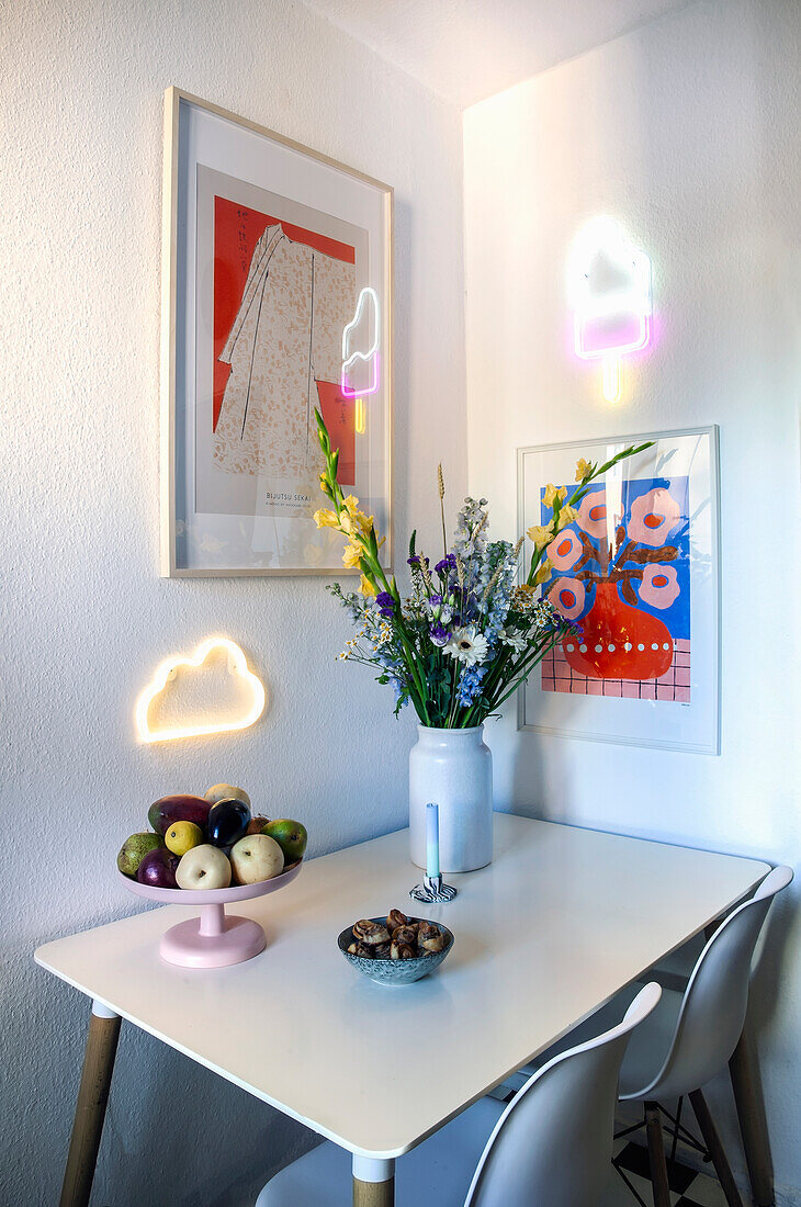 Esstisch mit Blumenvase, Obstschale und Neonschild an der Wand