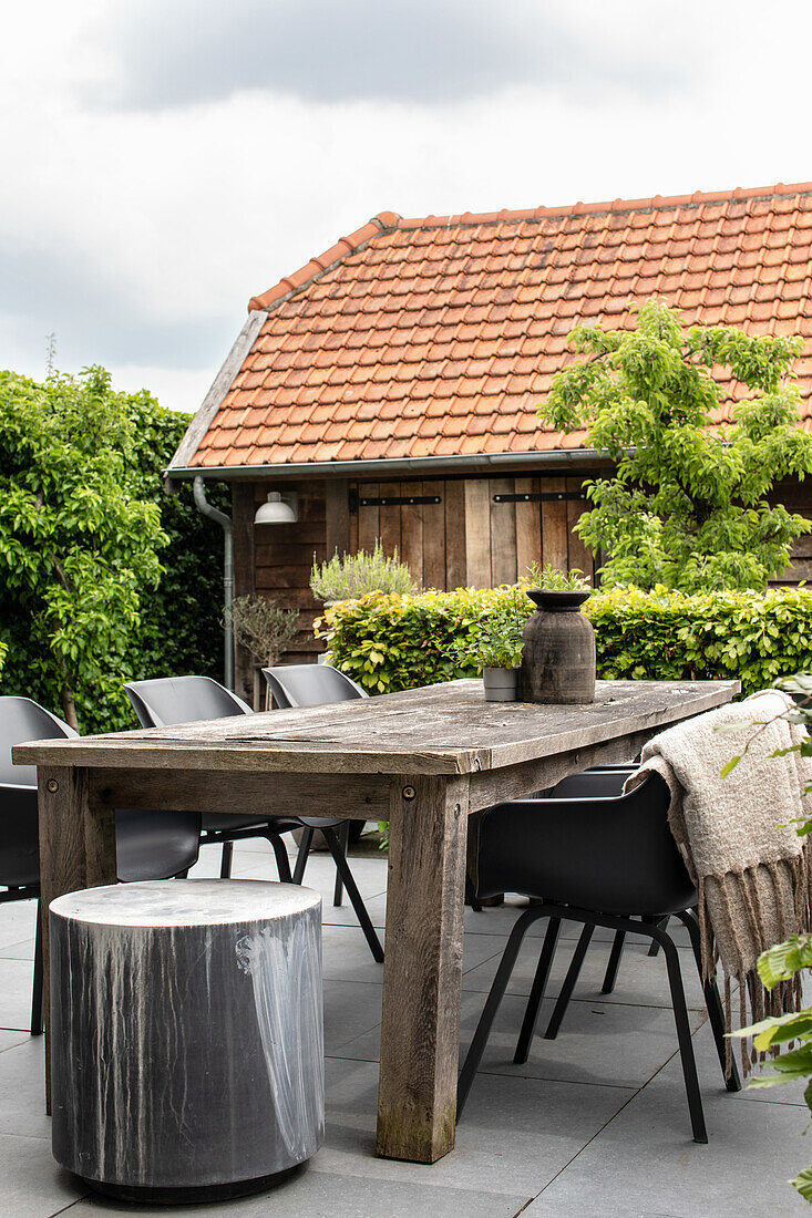 Terrasse mit rustikalem Holztisch und modernen Stühlen vor alter Scheune