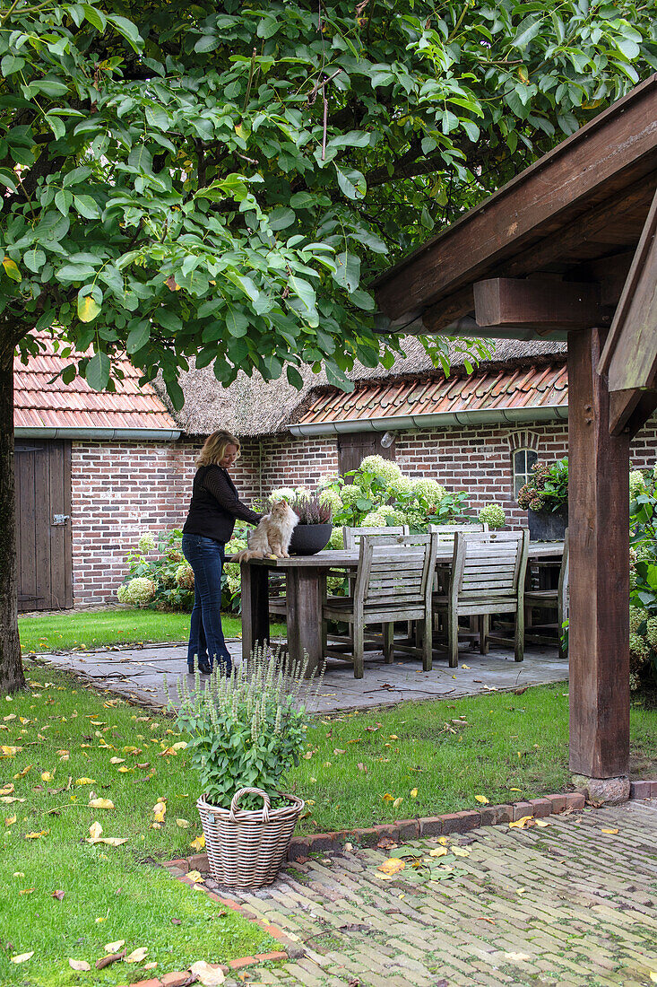 Frau streichelt Katze auf Terrasse mit Holzmöbeln und Schale mit Lavendelpflanzen