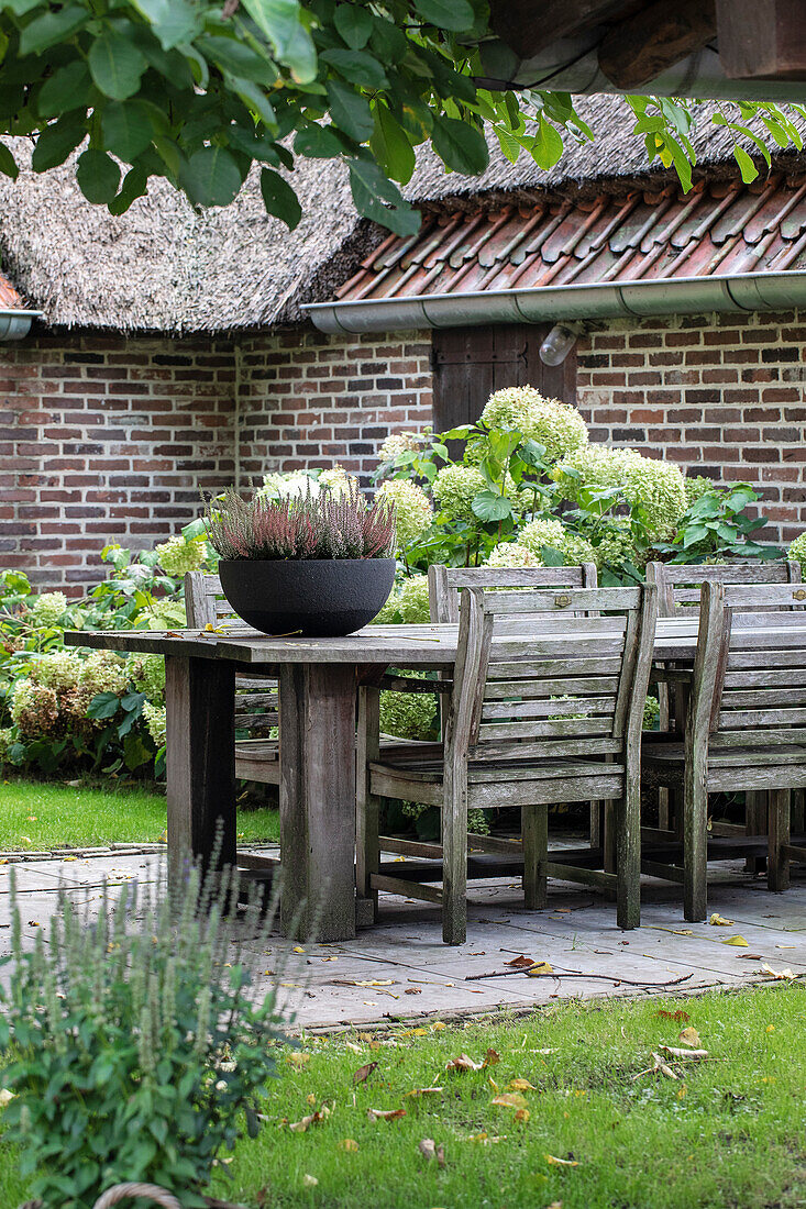 Holztisch mit Stühlen und Blumenarrangement auf Gartenterrasse