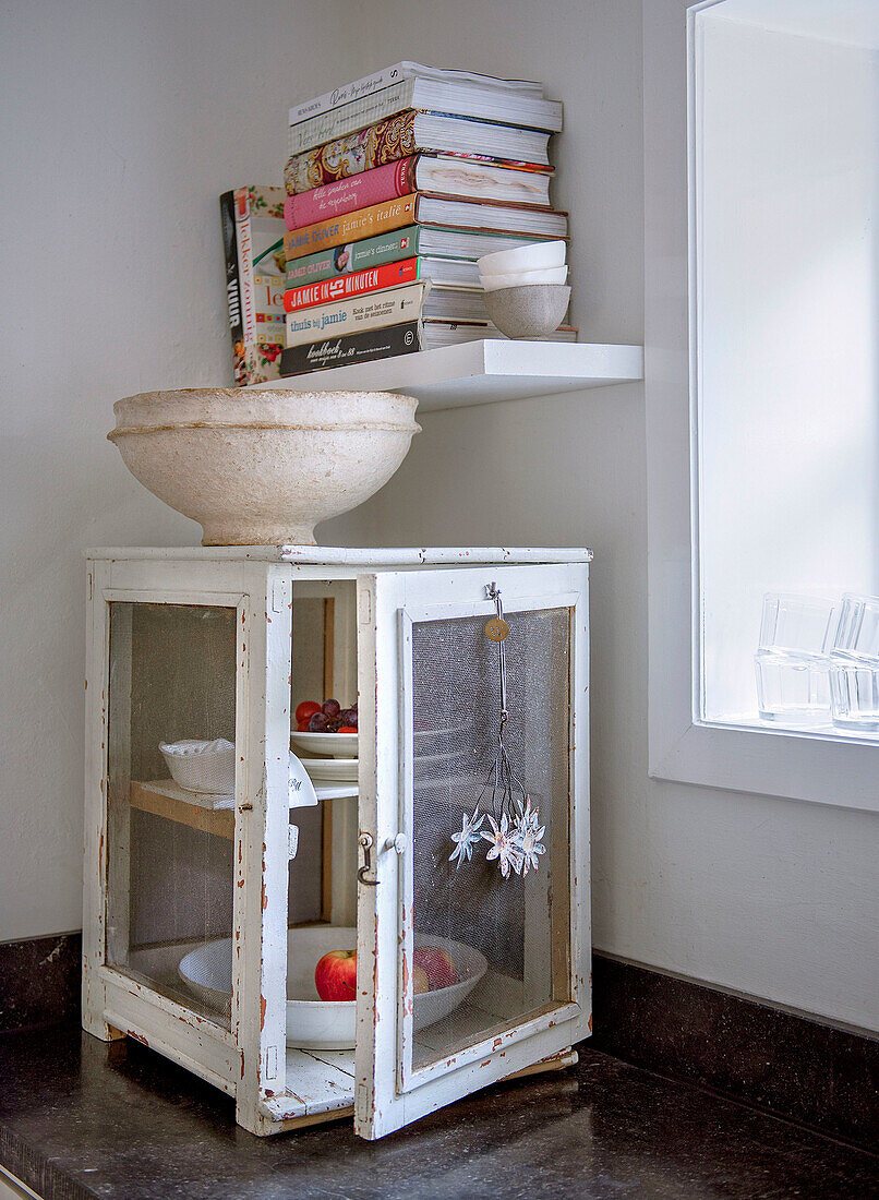 White vintage cupboard with glass fronts, bookshelf above