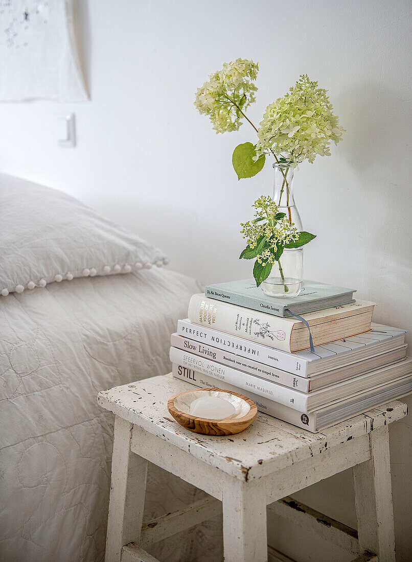 Weißer Nachttisch im Shabby-Chic-Stil mit Bücherstapel und Hortensie in Glasvase