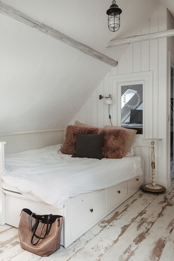 Cosy bed with storage space under a sloping roof with white wood panelling