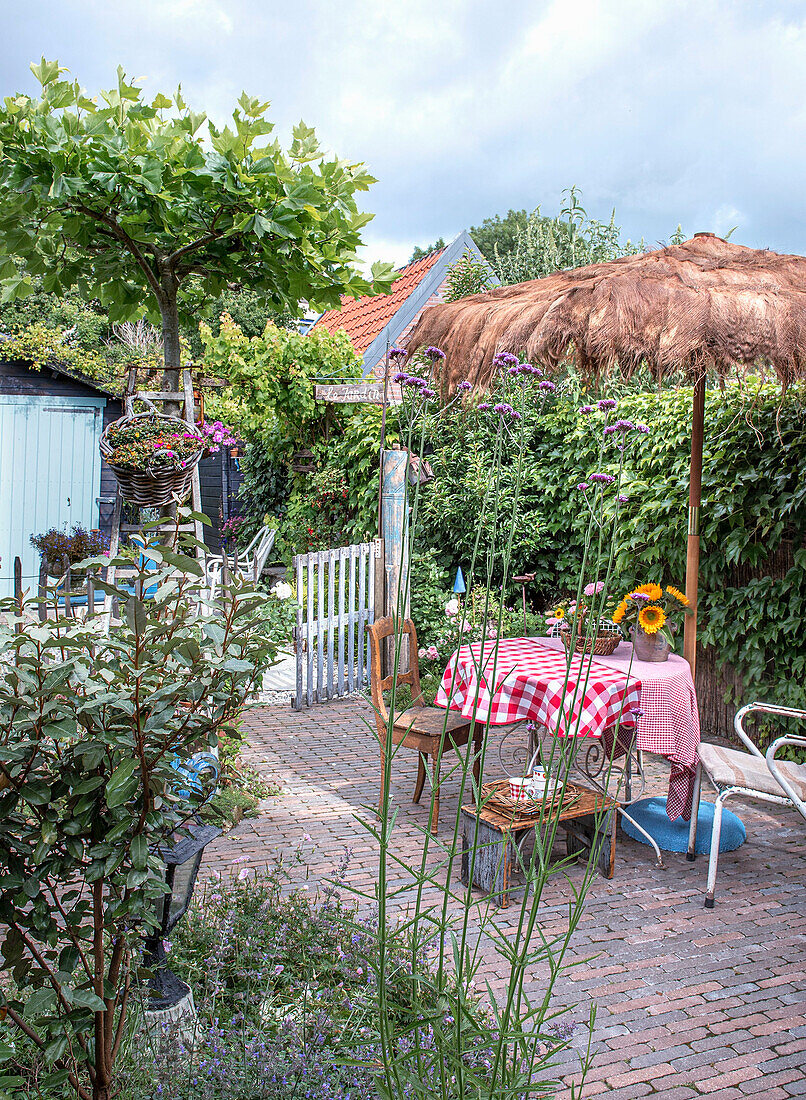 Idyllischer Gartenbereich mit schattenspendendem Strohdach und kariertem Tischdecken