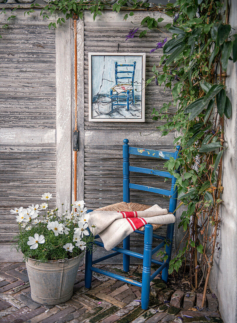 Blue wooden chair and metal flower pot in front of weathered wooden wall