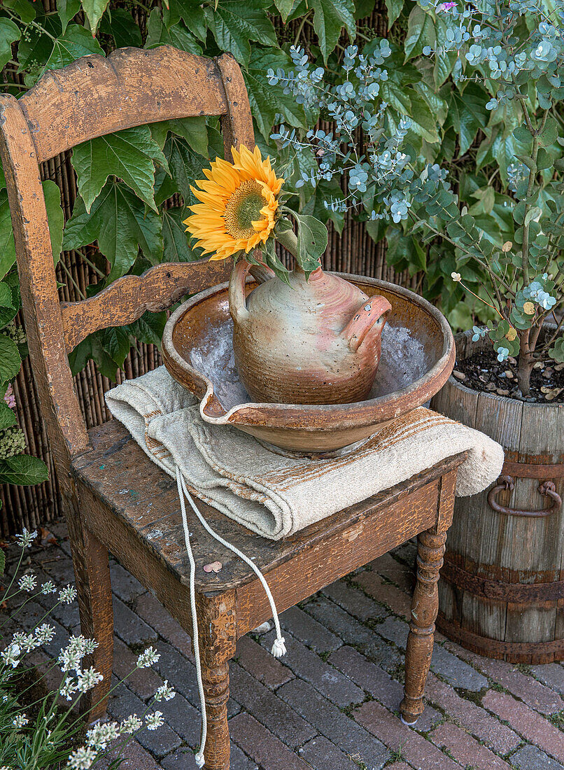 Tonkrug mit Sonnenblume (Helianthus) auf rustikalem Eichenstuhl