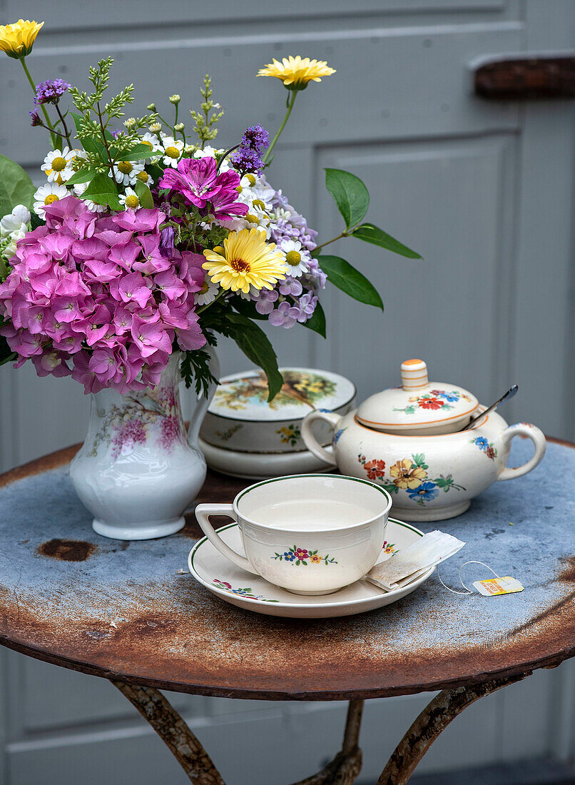 Tea service with floral pattern and bouquet of flowers on round garden table