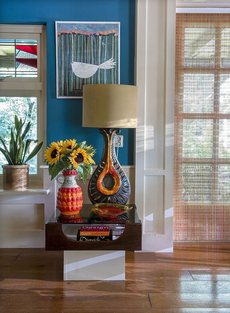 Side table with large lamp and bouquet of sunflowers in front of blue wall