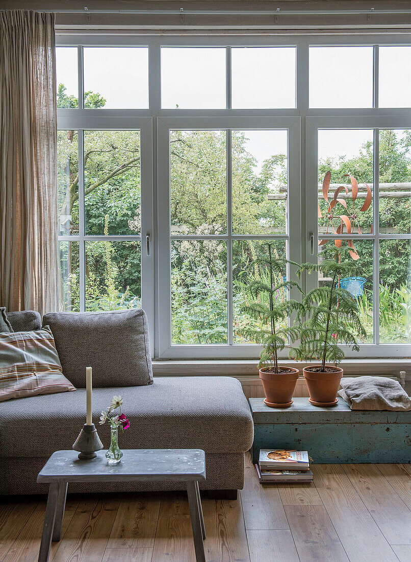 Wohnbereich mit großer Fensterfront, grauem Sofa und rustikalem Holztisch